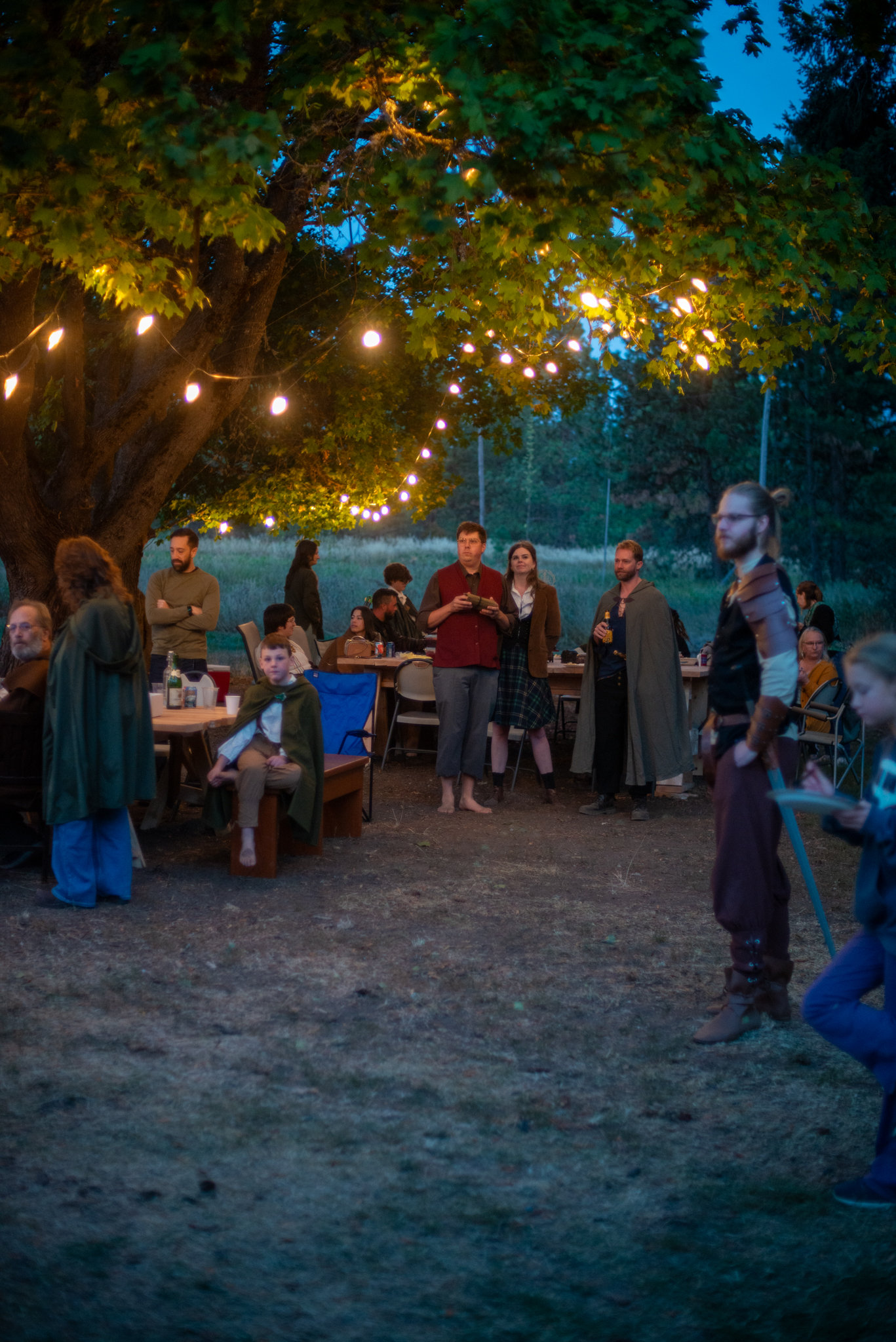 Costumed guests mingling beneath the lit party tree at blue hour
