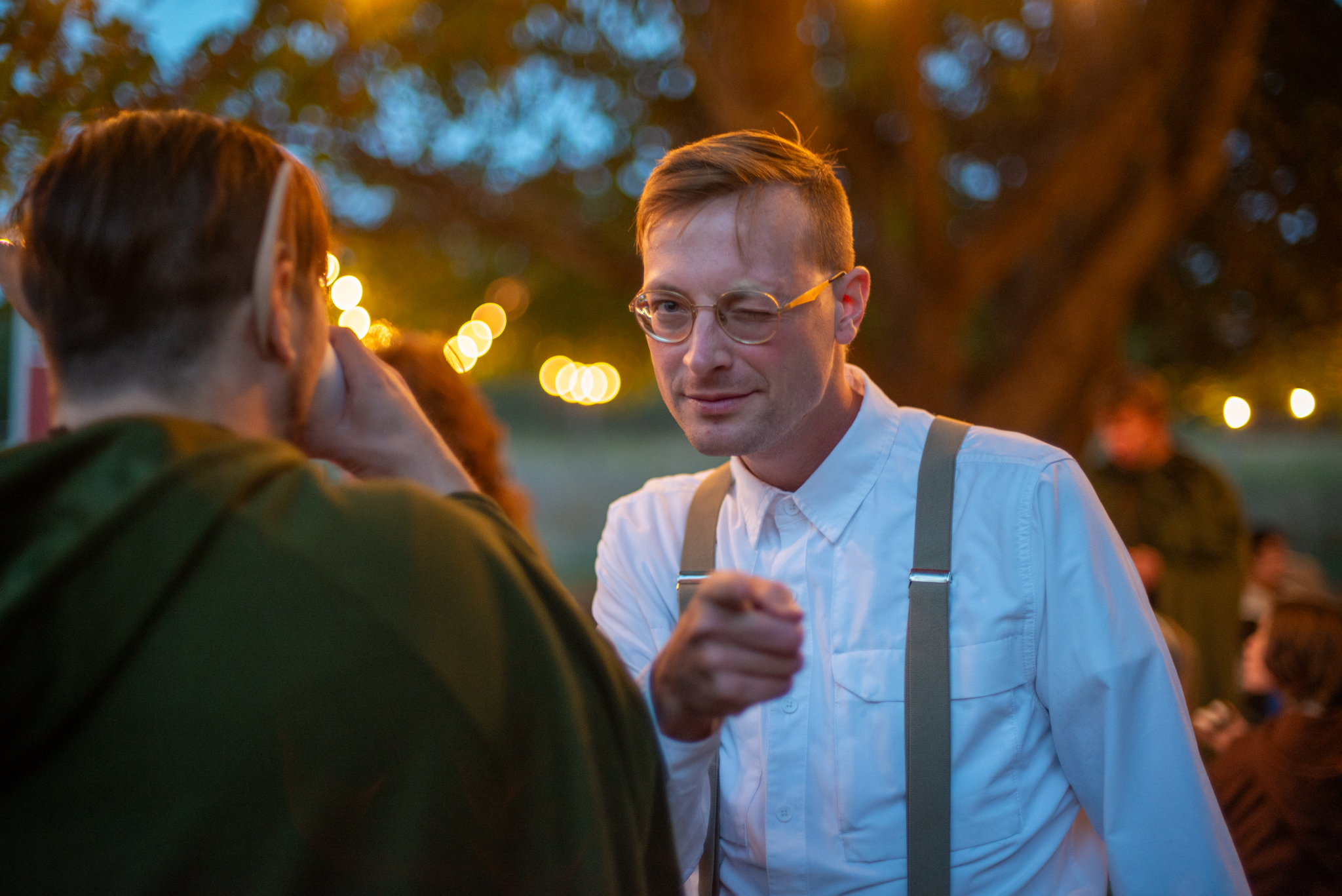A guest in shirtsleeves and suspenders sharing a joke by the string lights