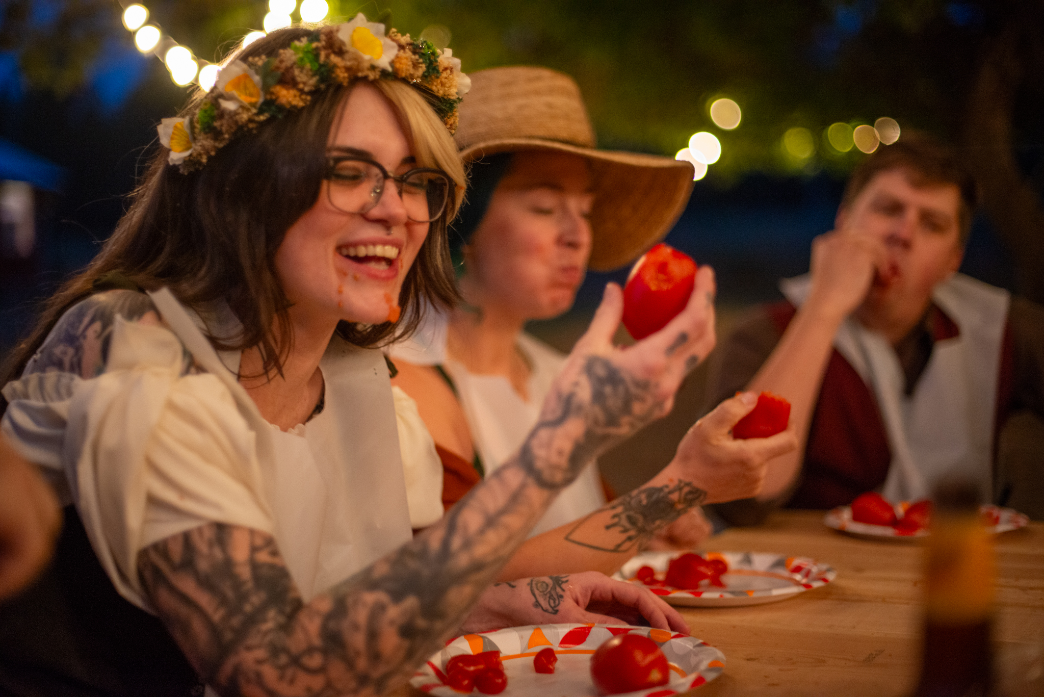 Laughing guests in bibs and flower crowns during a tomato-eating contest at the table